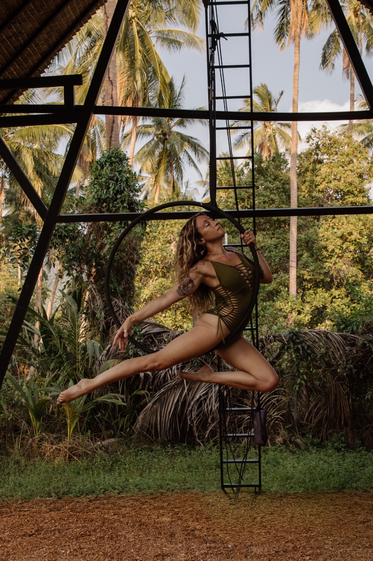 Melissa suspended in an aerial hoop framed by palms at golden hour